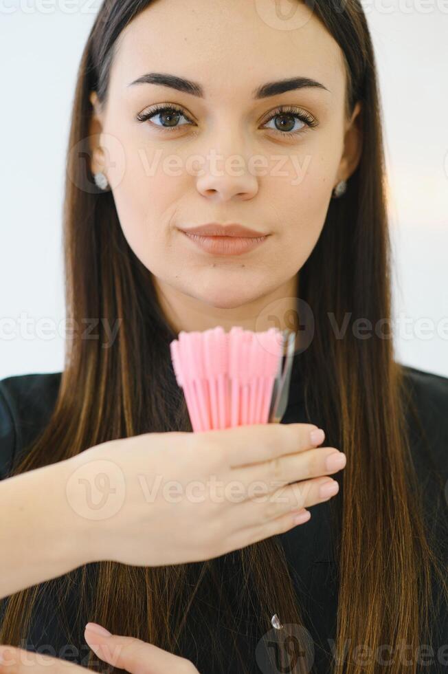 A beautiful woman, an employee of a beauty studio, holds eyebrow brushes in her hands. photo