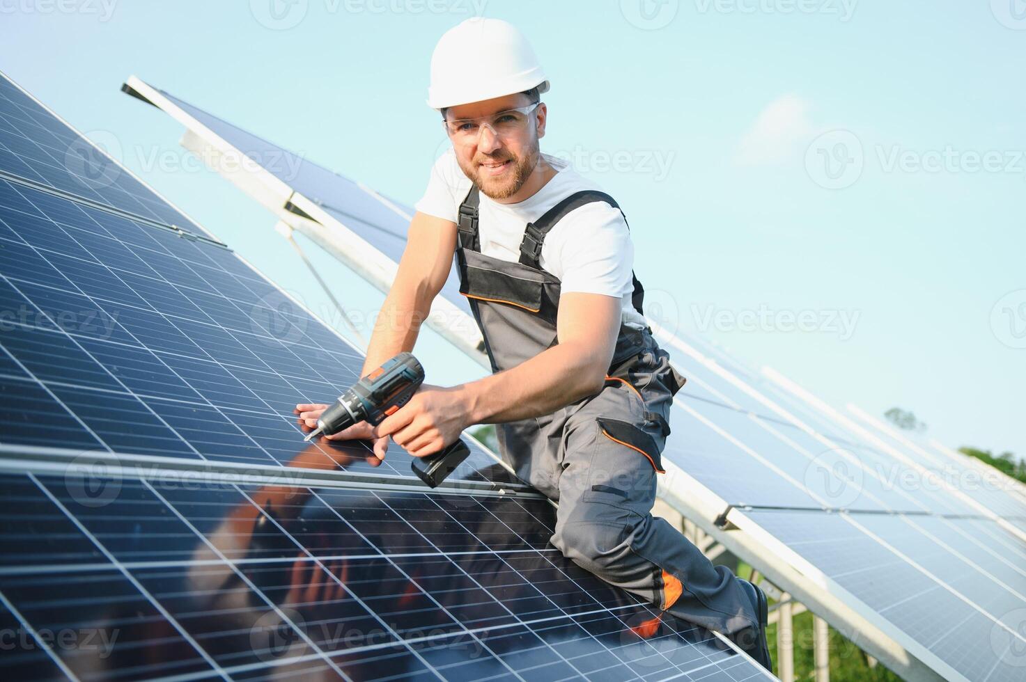 Male worker in uniform with a drill - screwdriver in his hand on a stepladder near solar panels photo