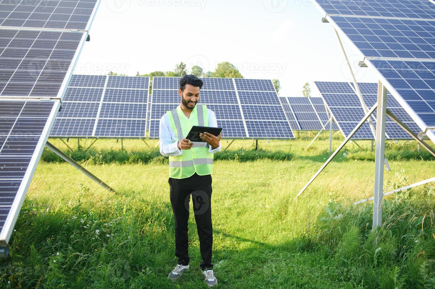 male engineer checks a photovoltaic solar plant and uses a recording tablet. Indian Man in uniform holding tablet. photo