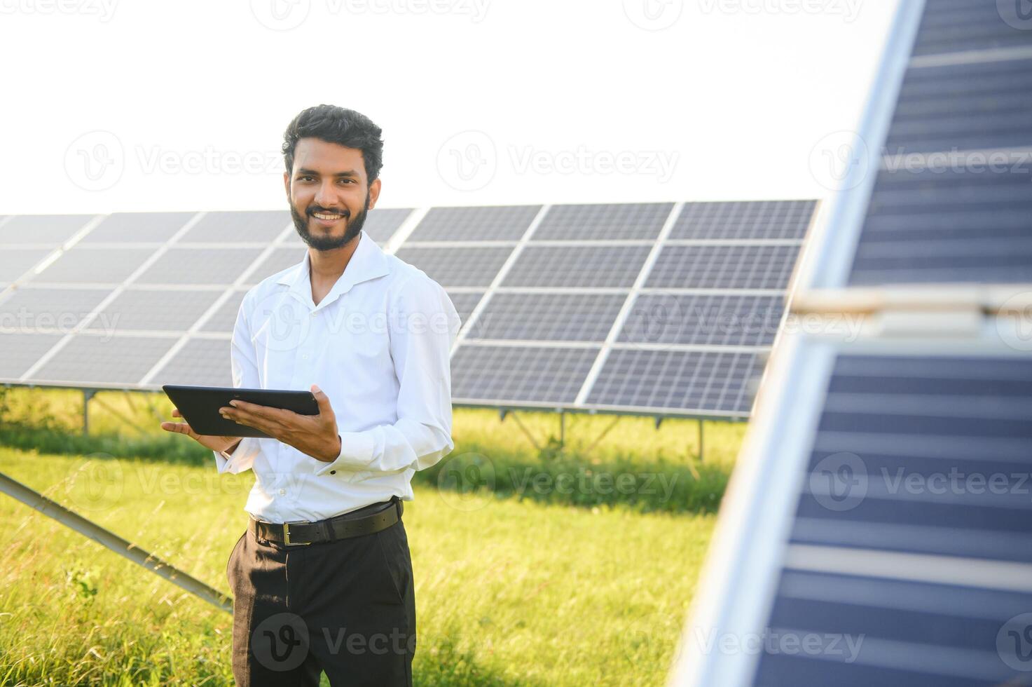 male engineer checks a photovoltaic solar plant and uses a recording tablet. Indian Man in uniform holding tablet. photo