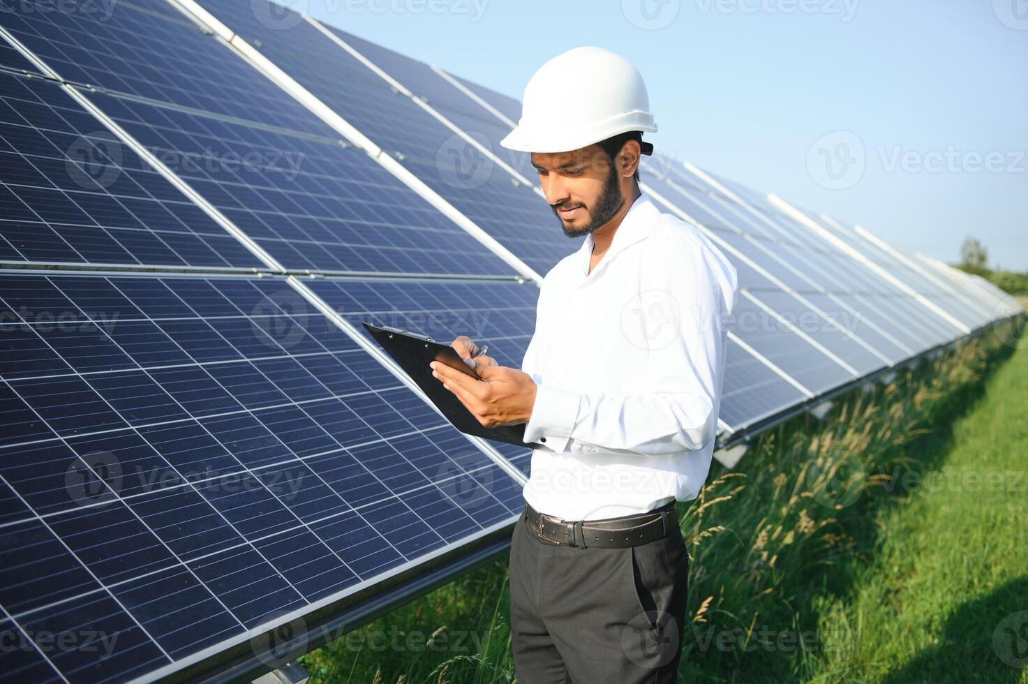 male engineer checks a photovoltaic solar plant and uses a recording tablet. Indian Man in uniform holding tablet. photo