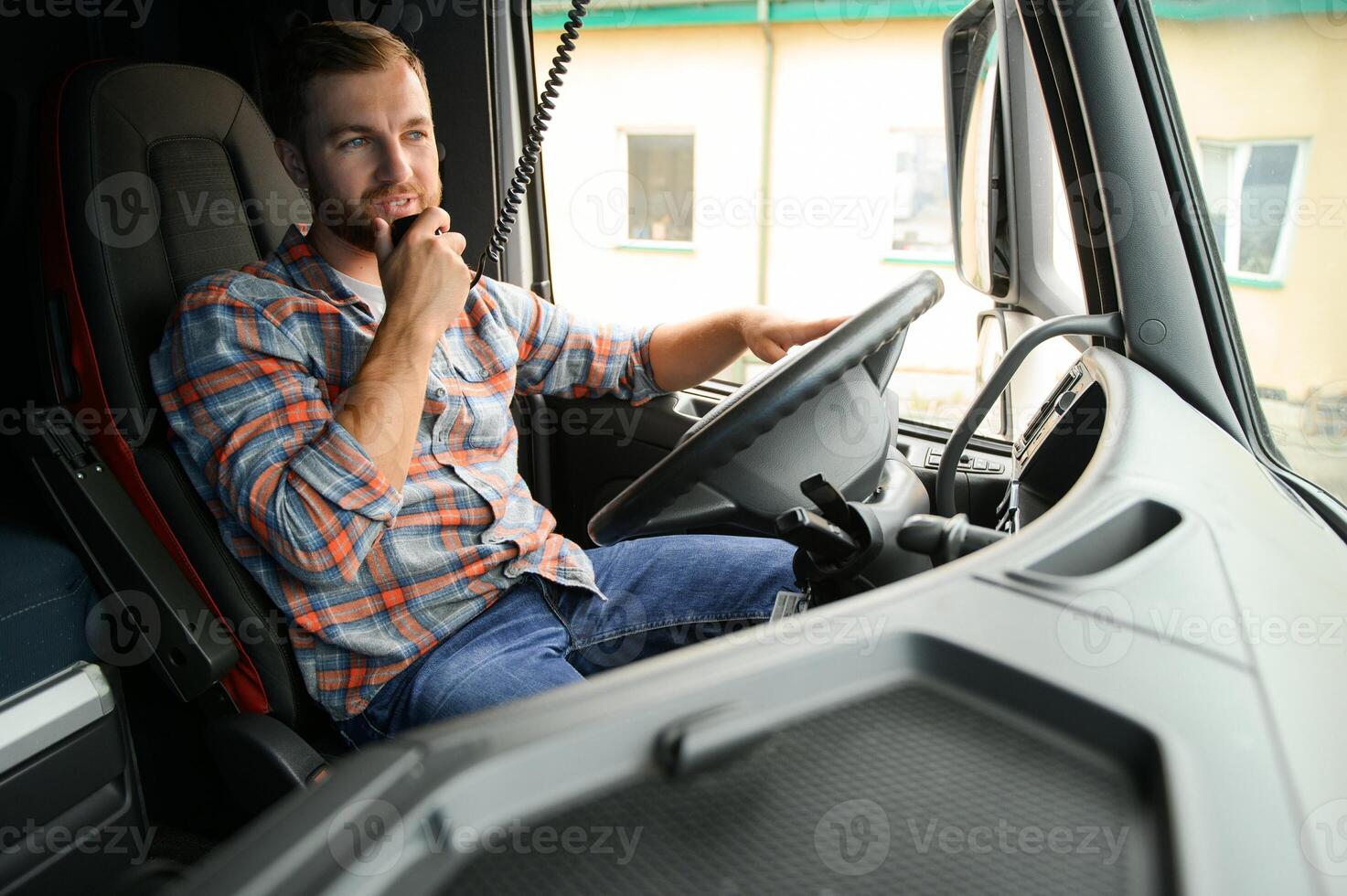 Man trucker driving in a cabin of his truck and talking on radio transmitter. photo