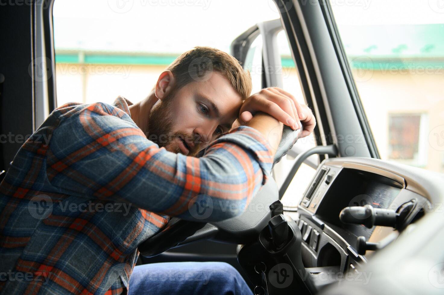 Tired of work. Sitting in the cabin. Young truck driver is with his vehicle at daytime. photo
