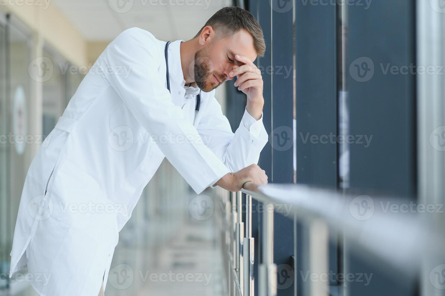 Sad doctor leaning against the wall in hospital corridor. photo