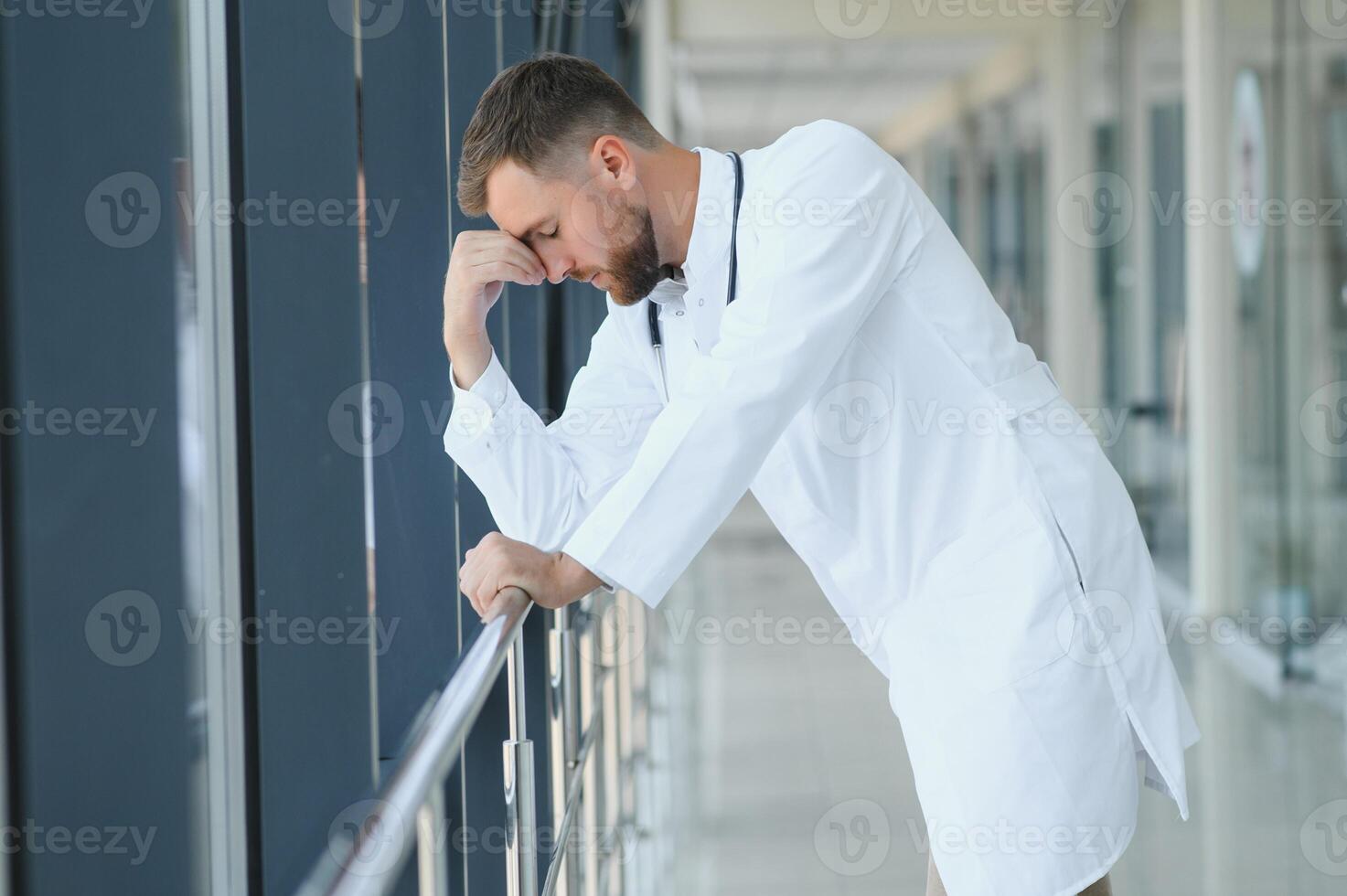 Sad doctor leaning against the wall in hospital corridor. photo