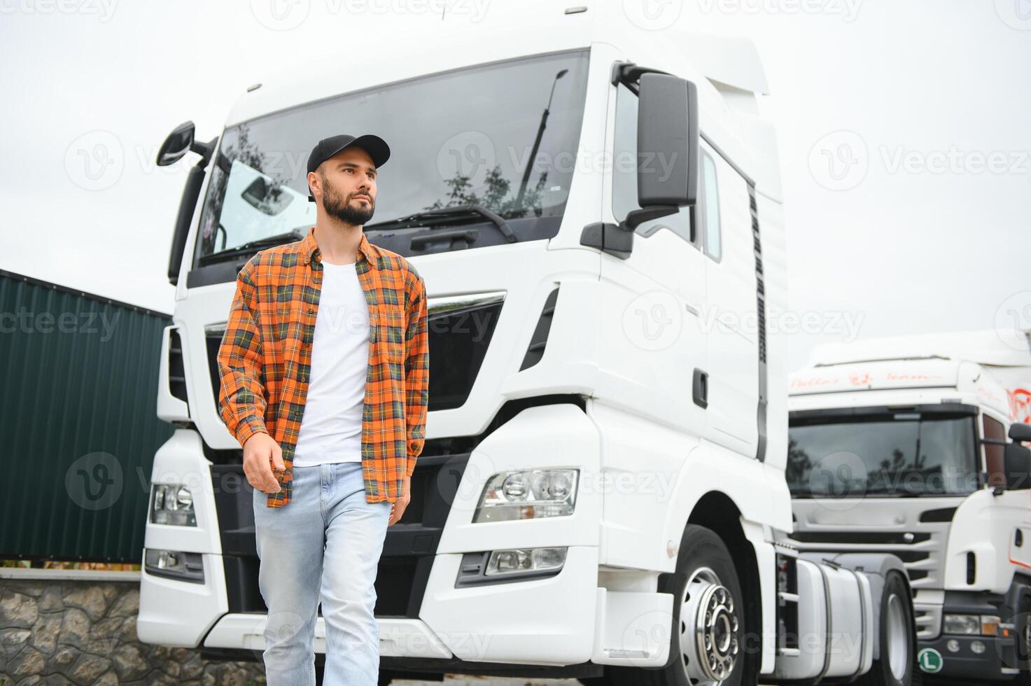 Portrait of young bearded man standing by his truck. Professional truck driver standing by semi truck vehicle. photo