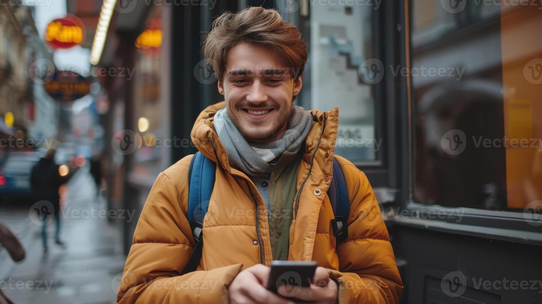 Smiling Young Man Enjoying a Rainy Day While Texting on His Phone in a Busy Urban Street photo