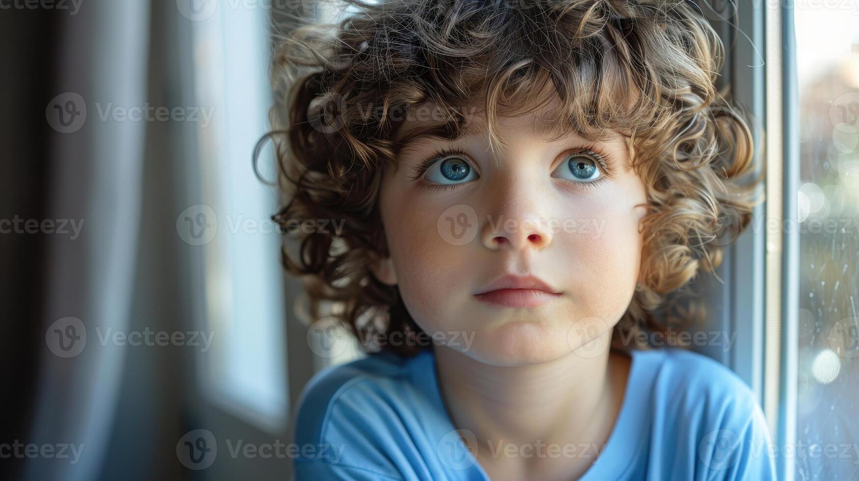 Contemplative Young Boy With Curly Hair Gazing Out of Bright Window in Late Afternoon Light photo