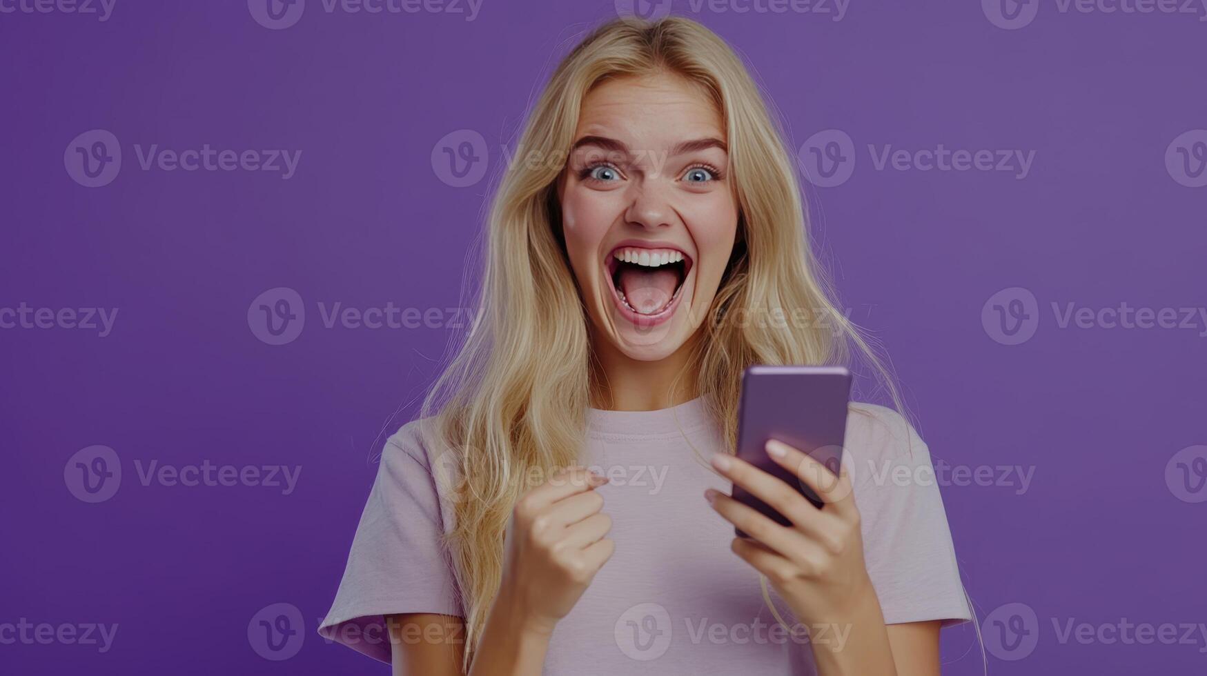 Excited Young Woman Celebrating While Holding Her Smartphone Against a Purple Background photo
