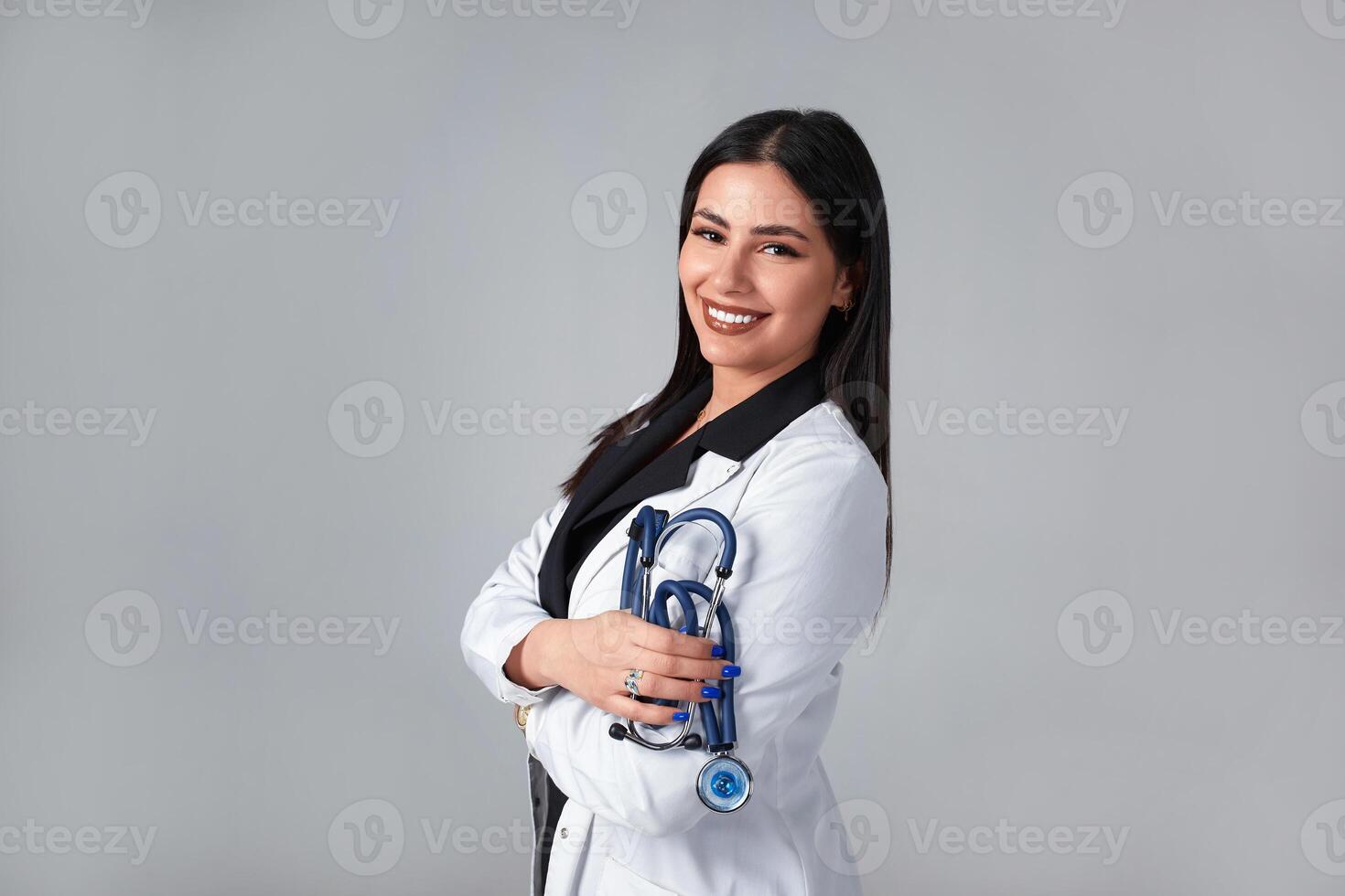 Medical concept of Brazilian beautiful female doctor in white coat with stethoscope, waist up. Medical student. Woman hospital worker looking at camera and smiling, studio, gray background photo