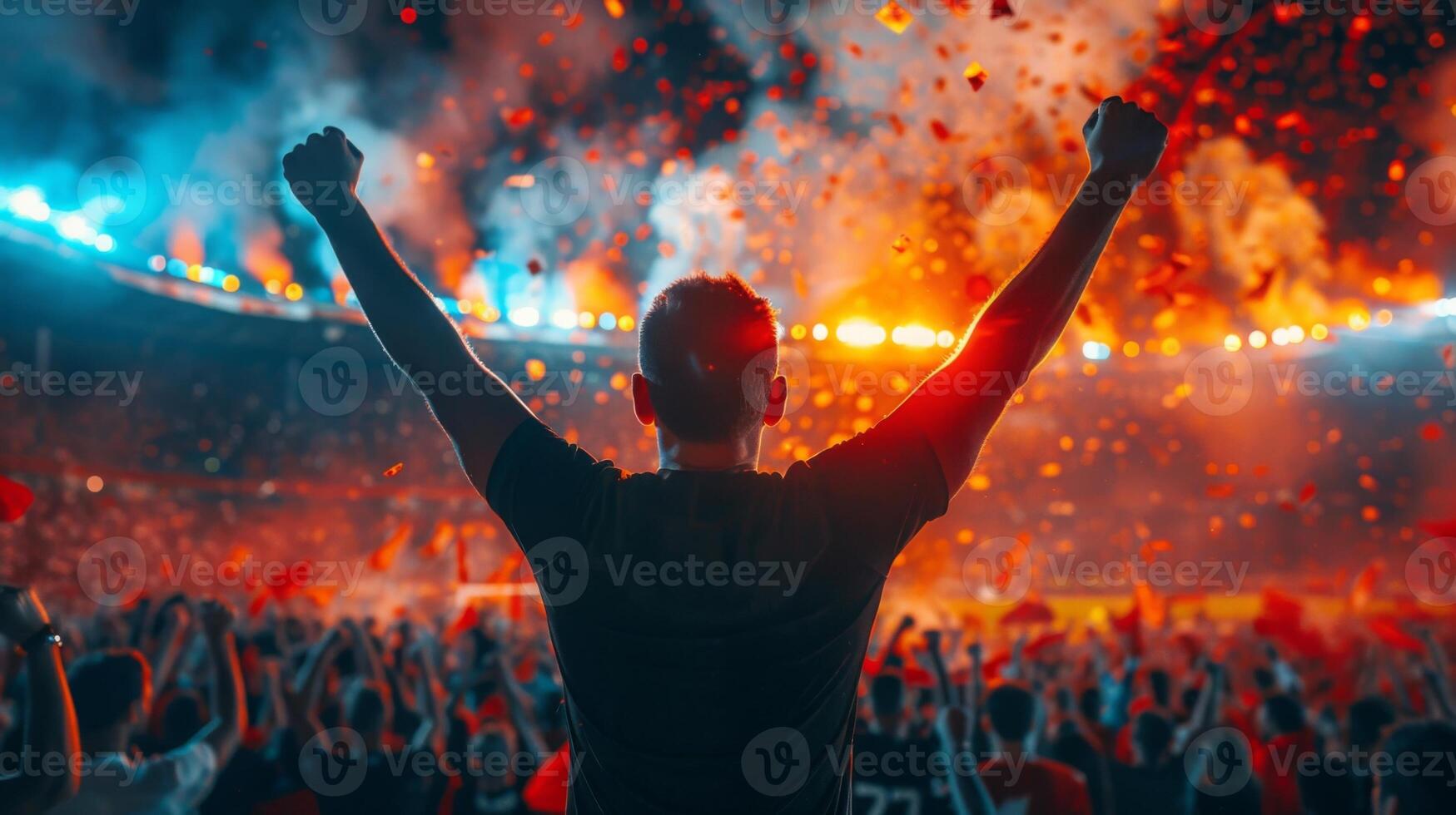 Man celebrates with arms raised in crowded night stadium as confetti falls from the sky photo