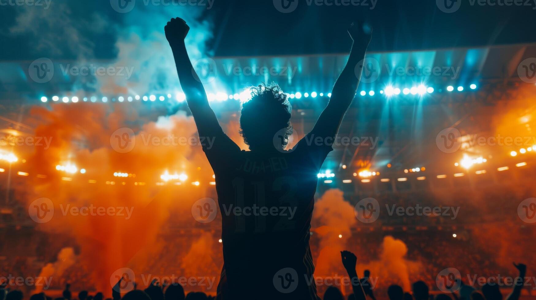 Soccer supporter raises his arms in excitement in a packed stadium at night photo
