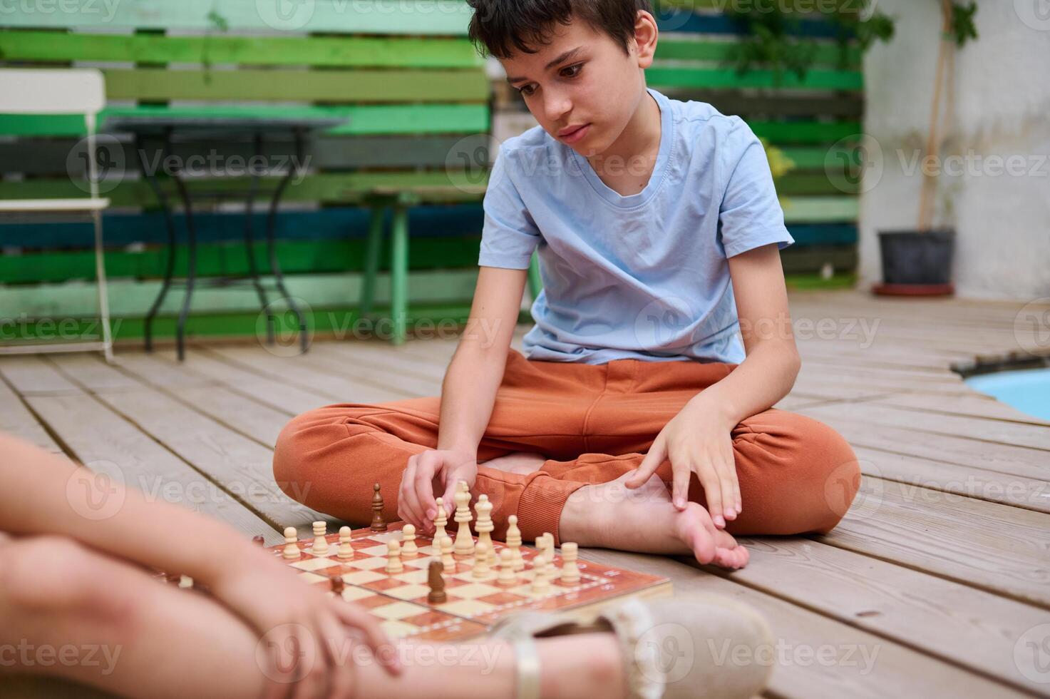 Young boy playing chess outdoors with a friend, focused and deep in thought photo