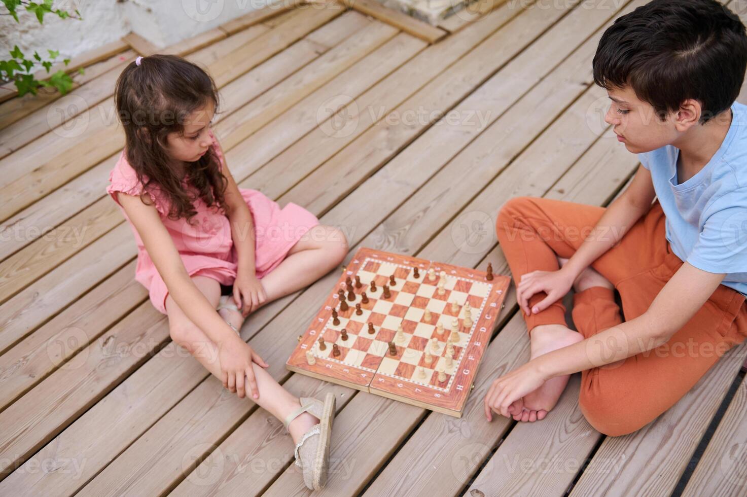 Children playing chess on a wooden deck on a sunny day, developing strategy and patience photo