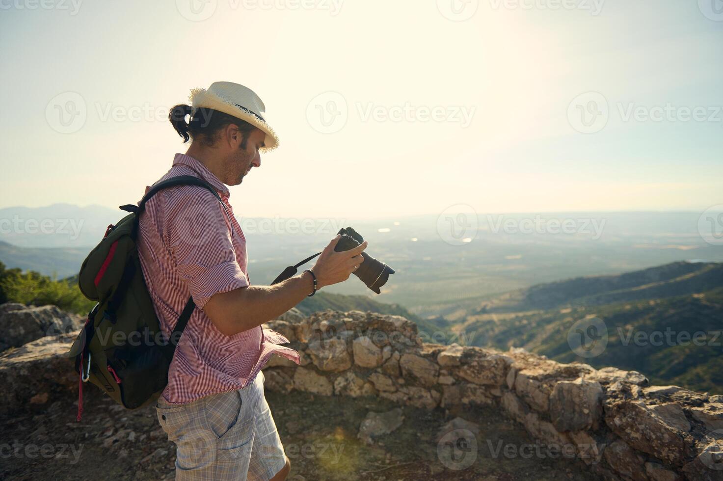 Man with hat and backpack taking photos of scenic mountain landscape on a sunny day