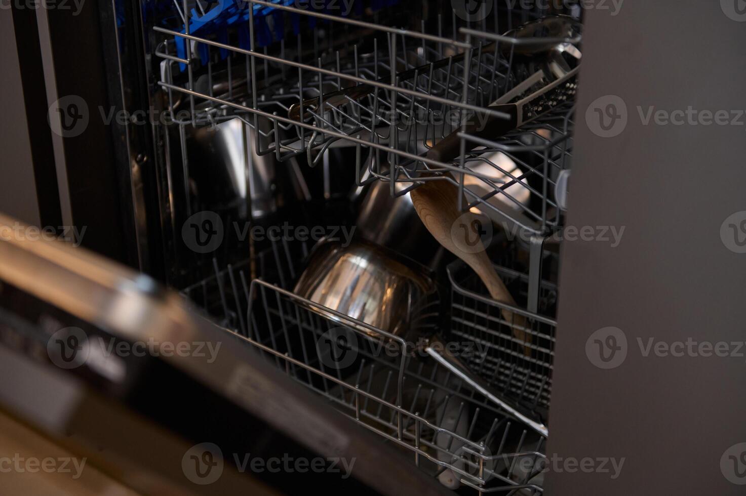 Open dishwasher loaded with kitchen utensils, pots, and wooden spoon photo