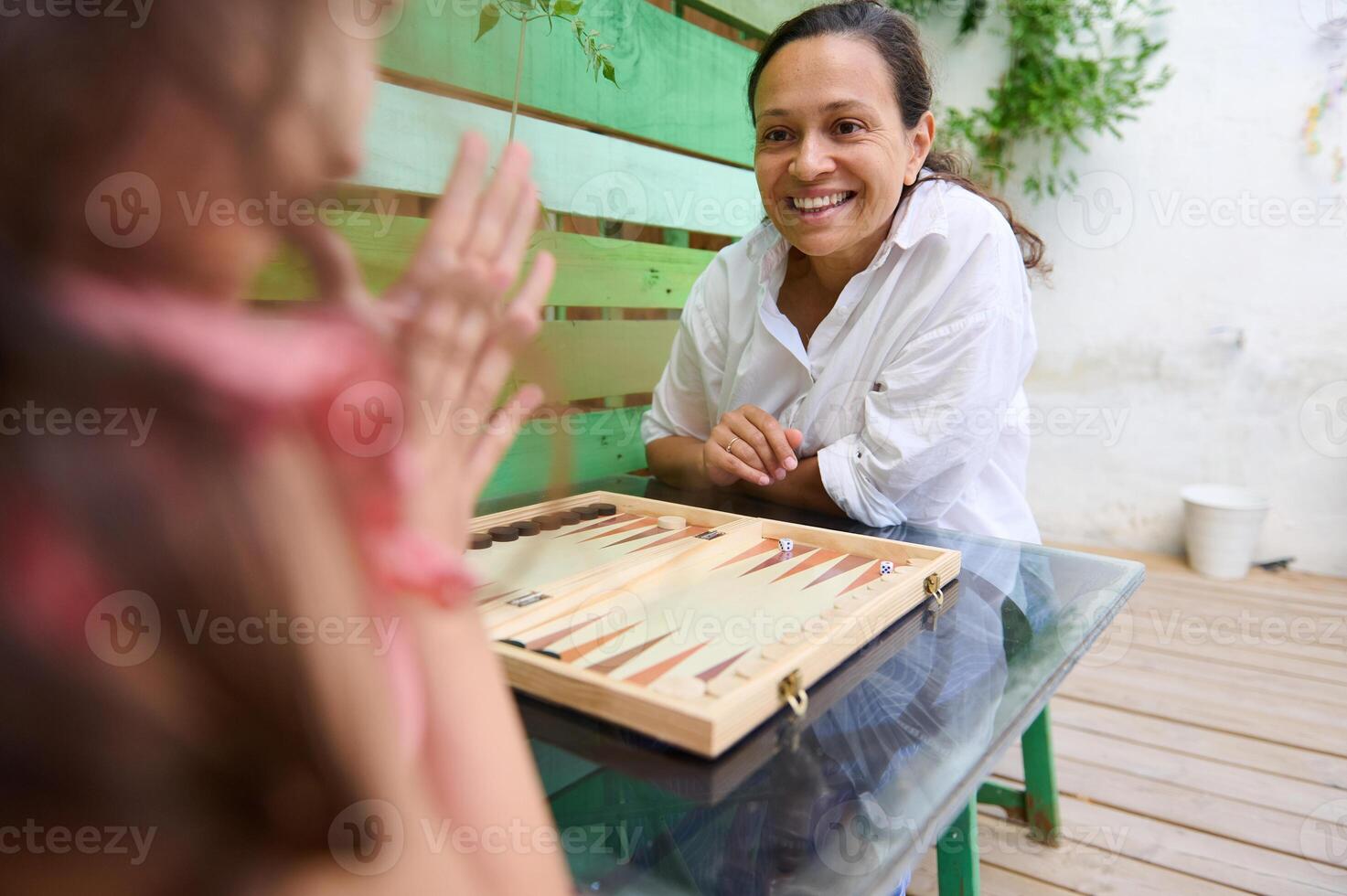 Mother and daughter playing board game on outdoor patio table and enjoying quality time photo