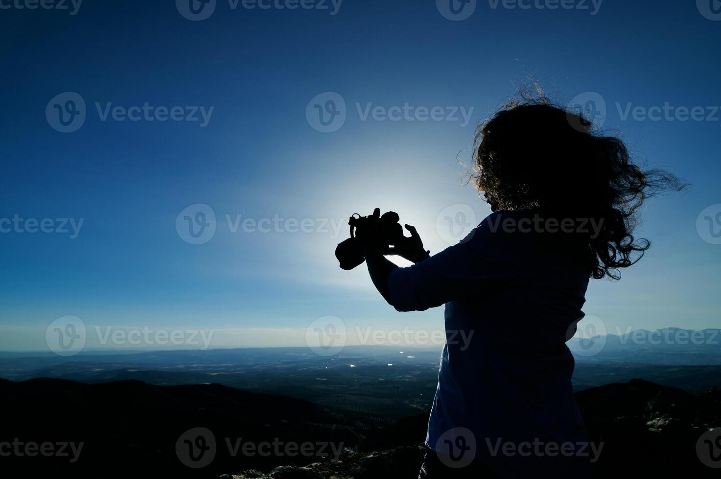 Silhouette of a woman photographing the scenic mountain landscape at sunset photo