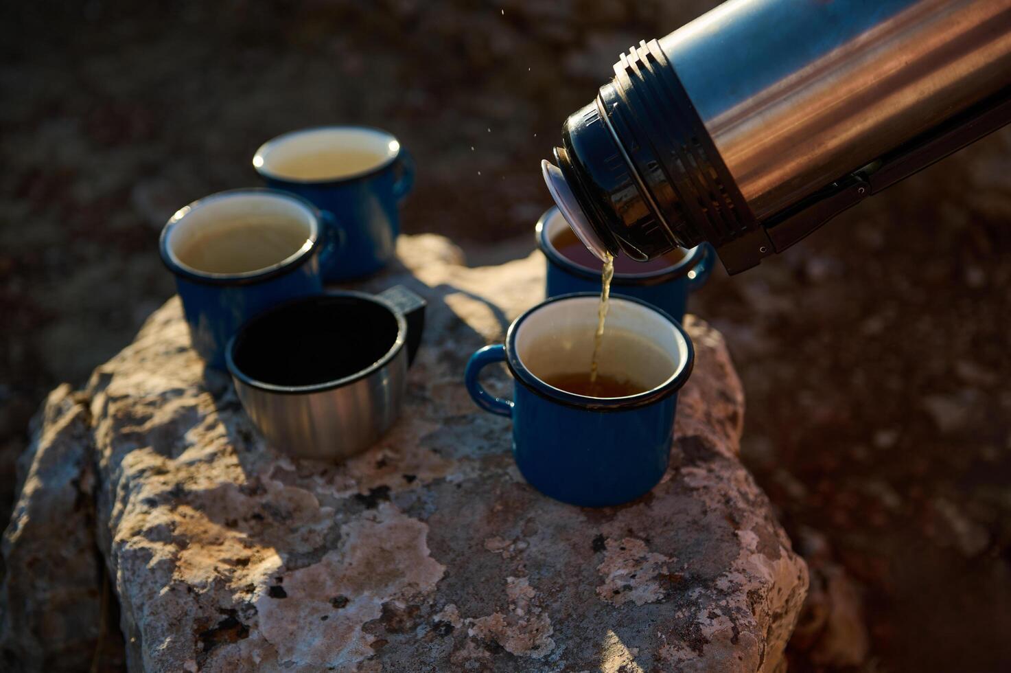 Pouring hot beverage into camping mugs on rocky surface outdoor adventure photo