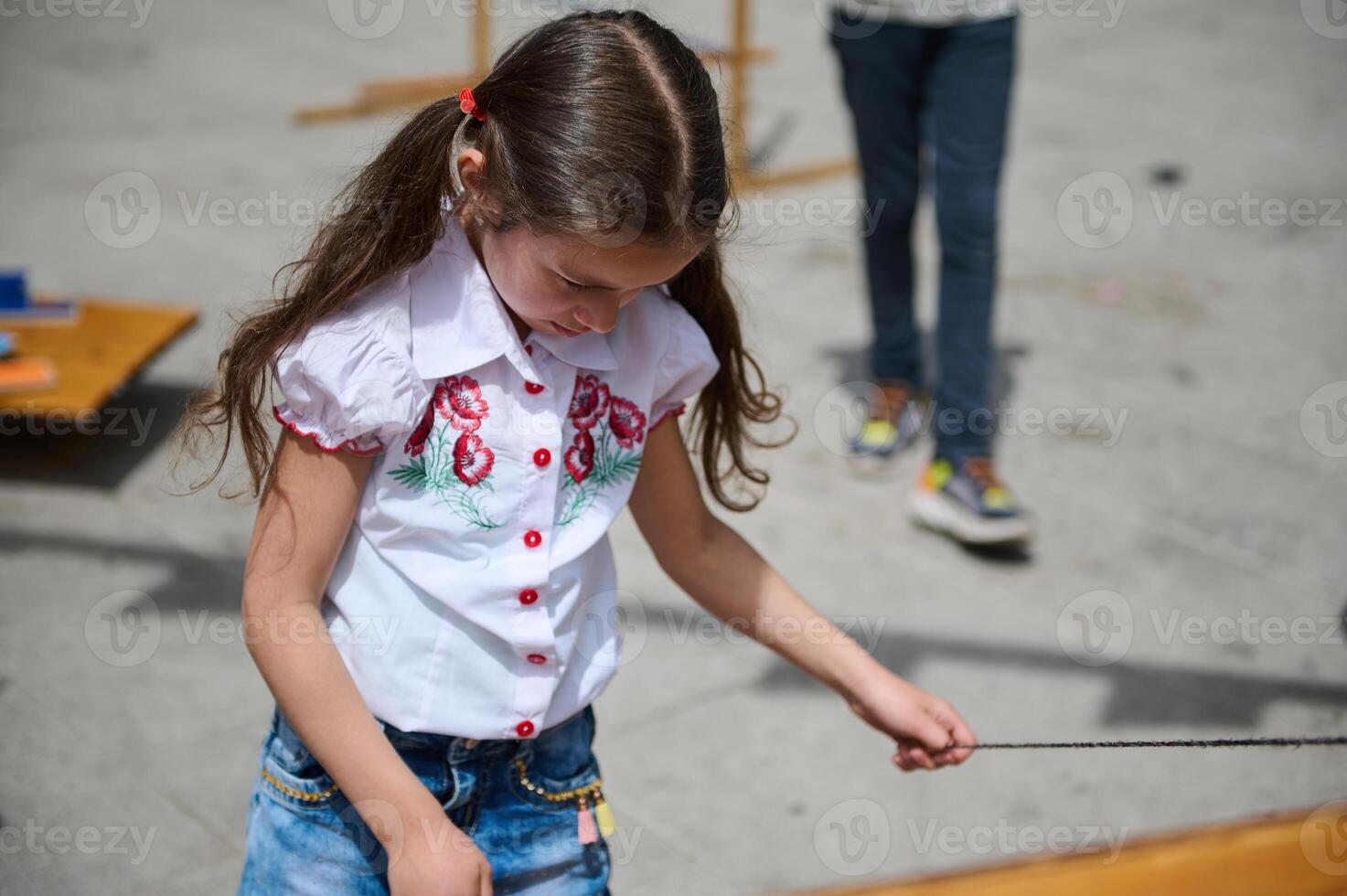 Young girl playing outdoors with string toy on a sunny day photo