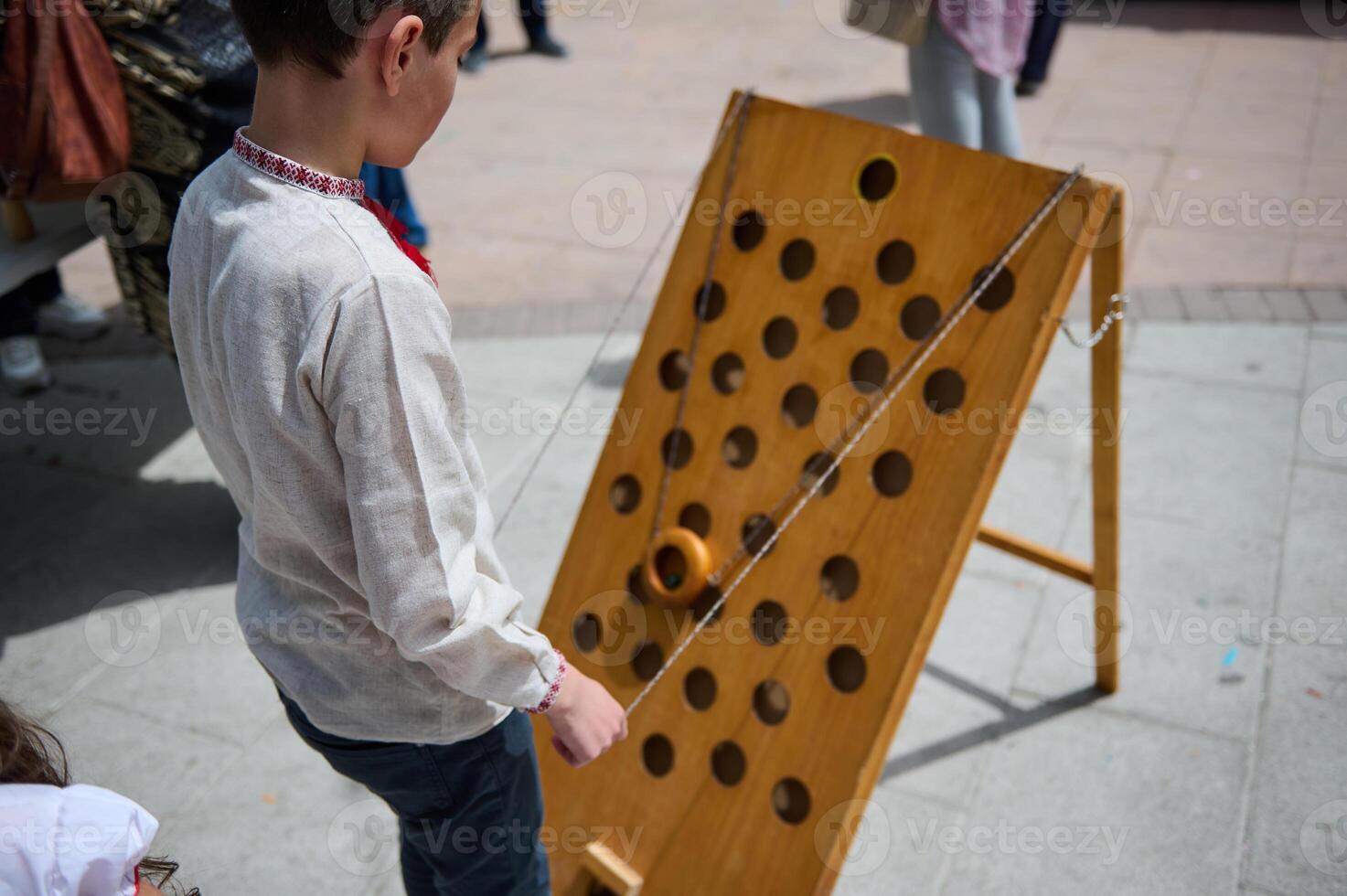 Child playing with wooden ring on string game at outdoor festival photo