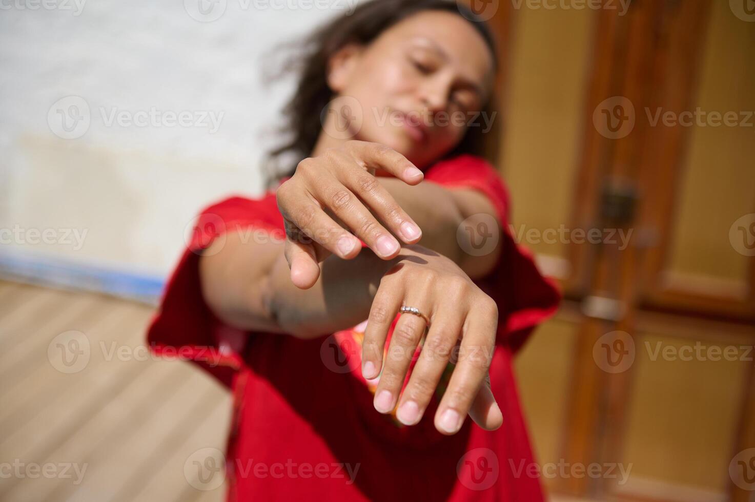 Relaxed woman stretching hands forward in natural sunlight wearing a red dress photo