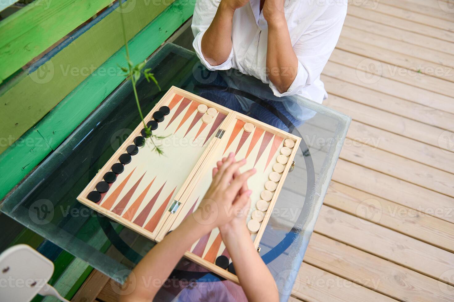 Two people playing backgammon outdoors on a wooden table, enjoying a casual game on a sunny day photo