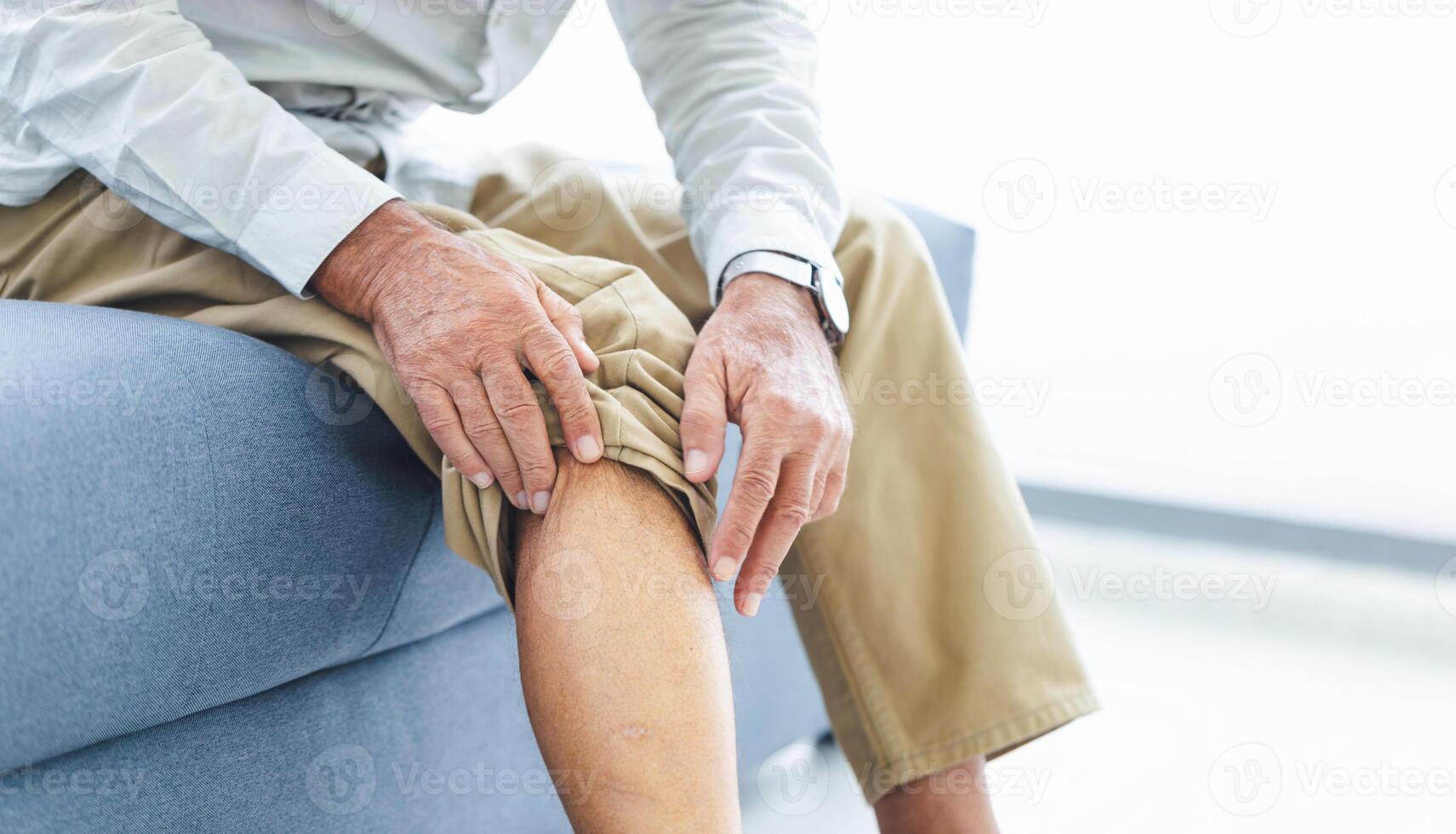 Senior man suffering from knee pain while sitting on the sofa, Old man suffering from knee pain sitting sofa photo