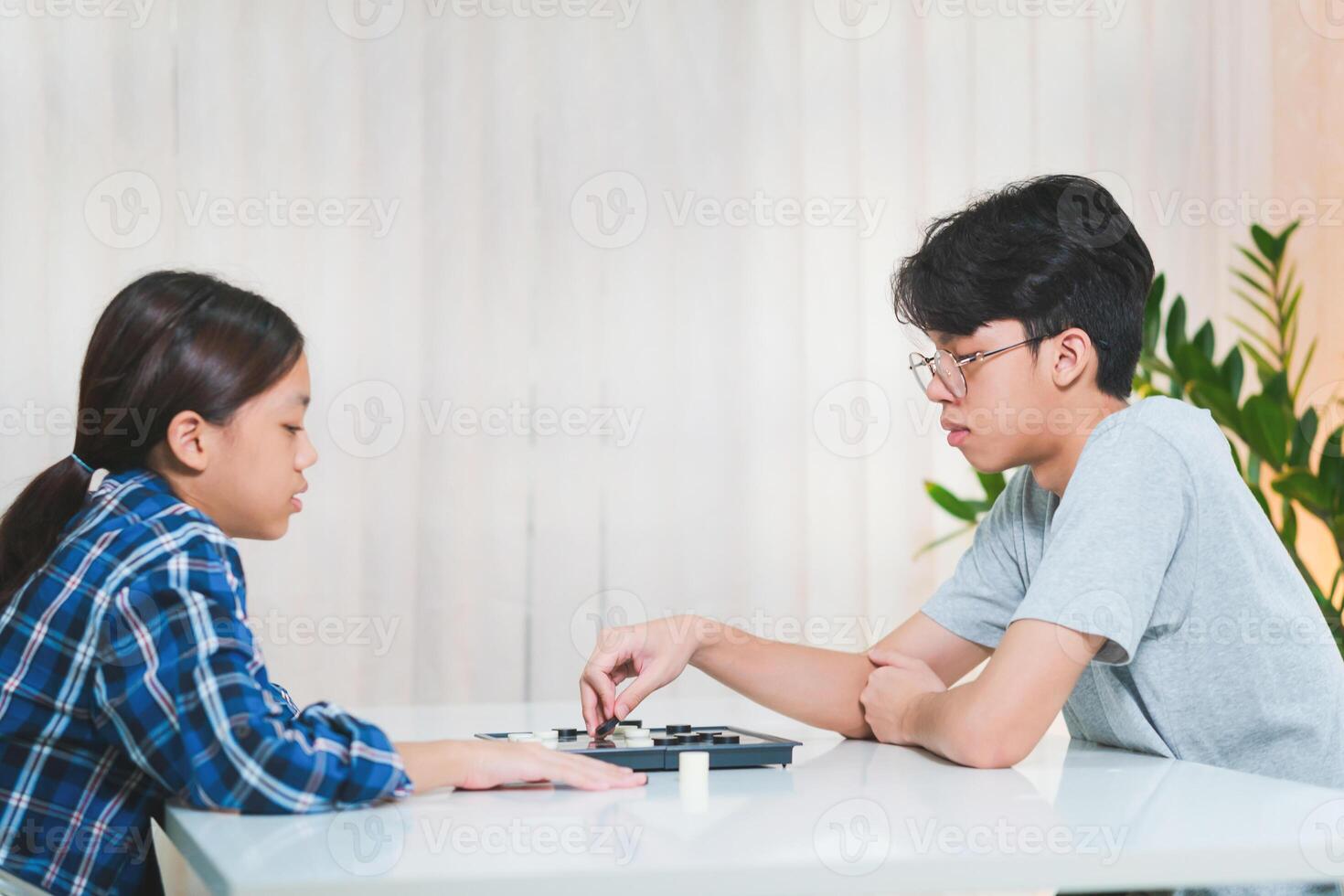 Asian teenage boy and girl playing board game, Asian brother and sister relaxing hobbies playing a game of checkers photo