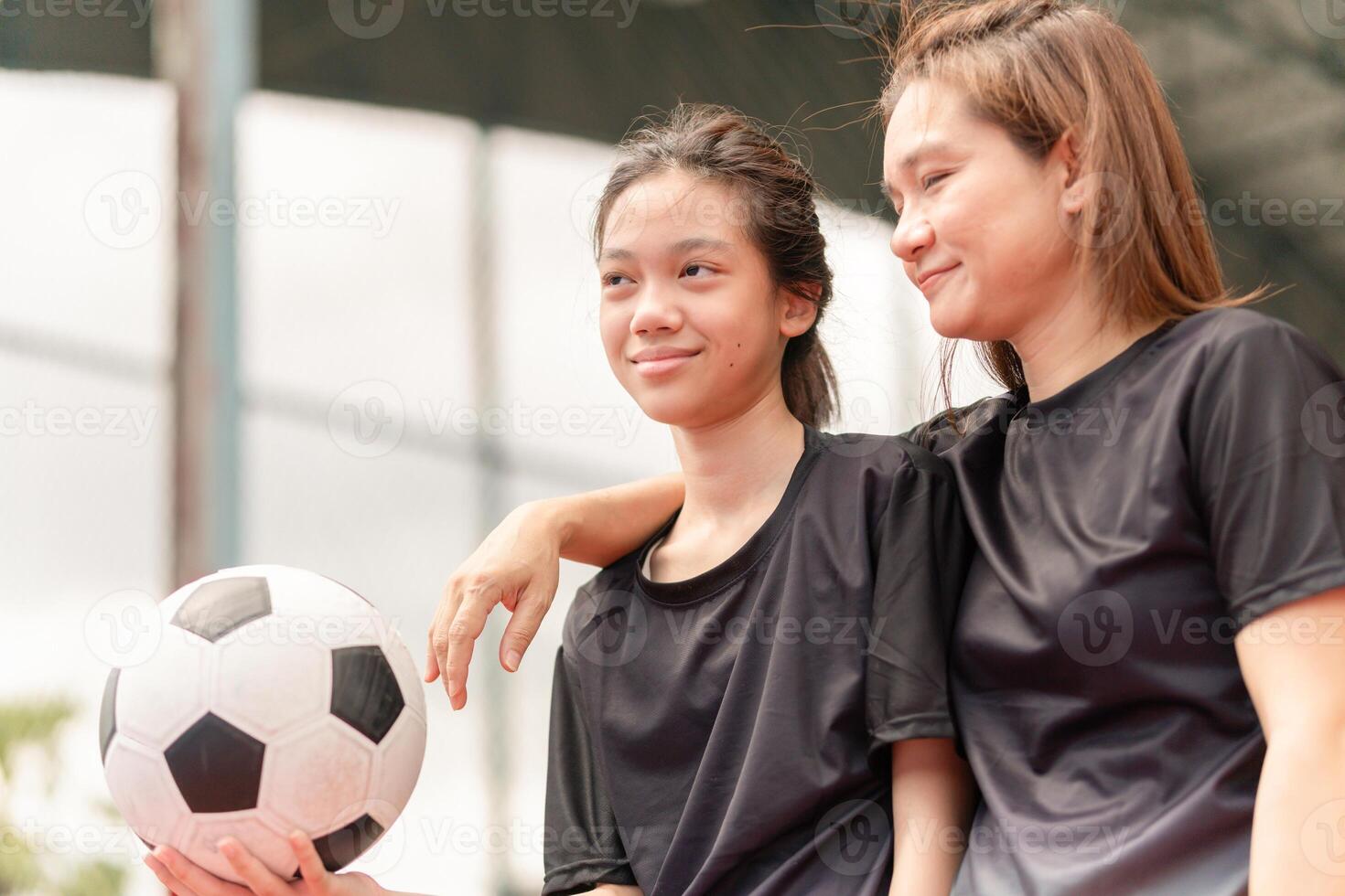 Asian child girl with soccer ball, Mother and daughter playing soccer, Mom with a child playing football in the urban outdoor futsal court photo