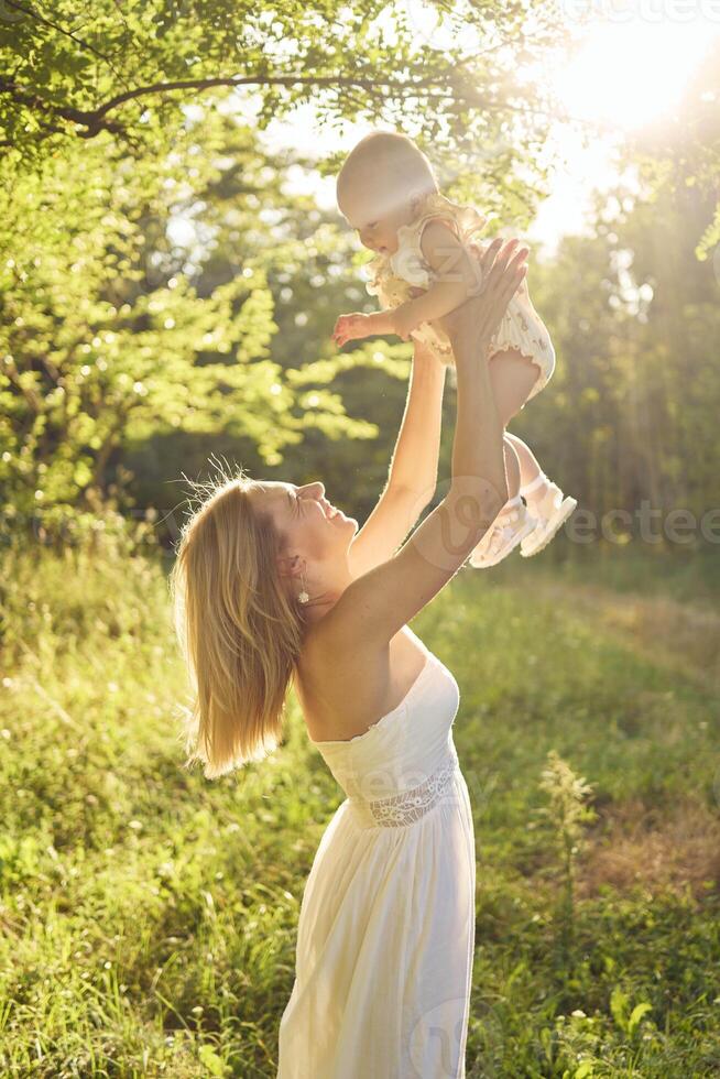 a mother plays with her baby daughter in a sunlit garden photo