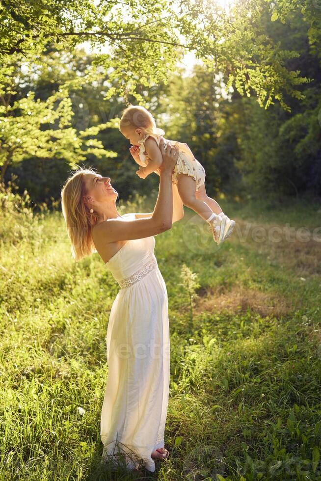 a mother plays with her baby daughter in a sunlit garden photo