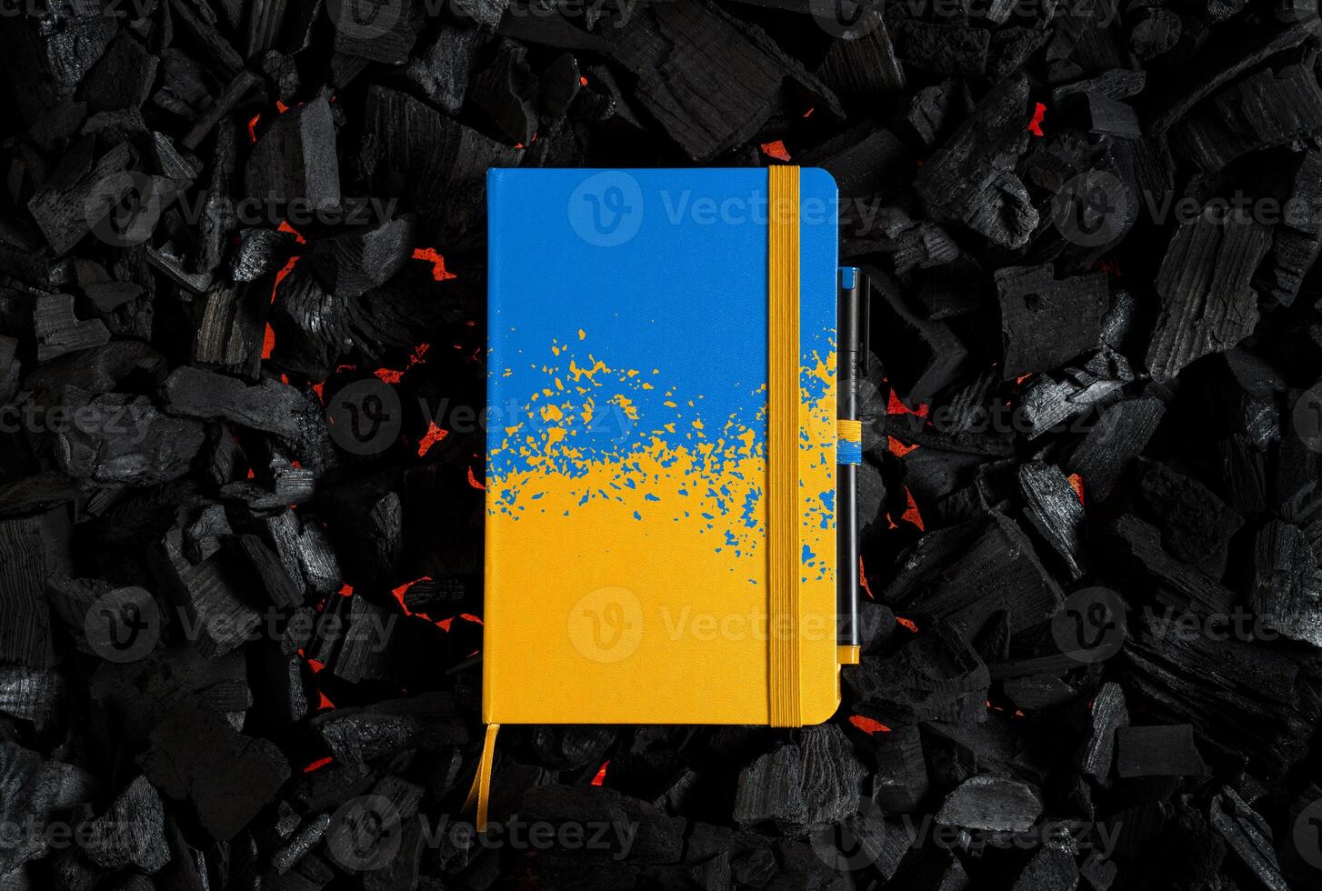 A small closed notebook with a yellow-blue cover in the colors of the Ukrainian flag. Texture of charcoal. Dark back photo