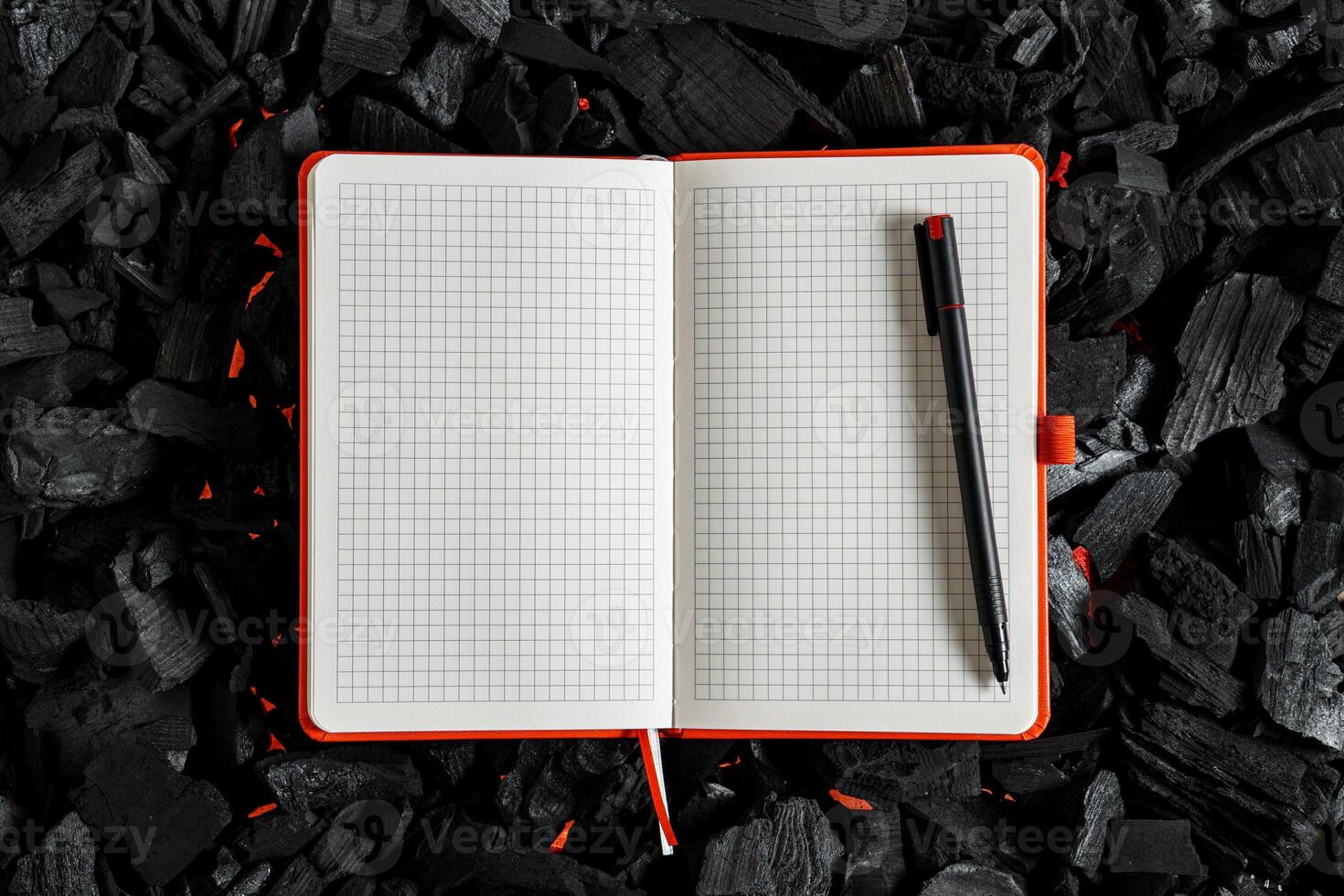 An open checkered notebook lying on a dark charcoal with red flashes of heat. photo