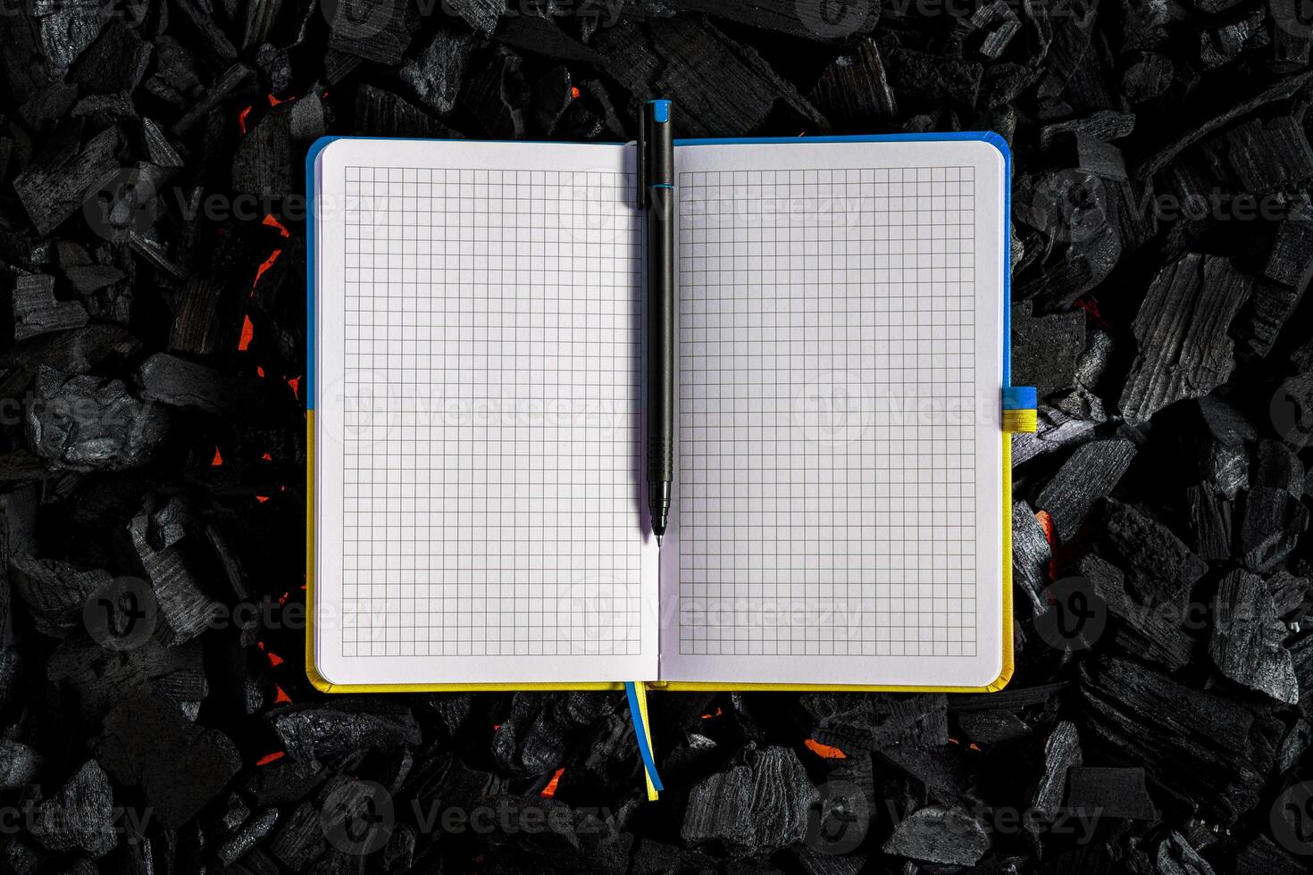 A small open notebook with a yellow-blue cover in the colors of the Ukrainian flag. Texture of charcoal. Dark back photo