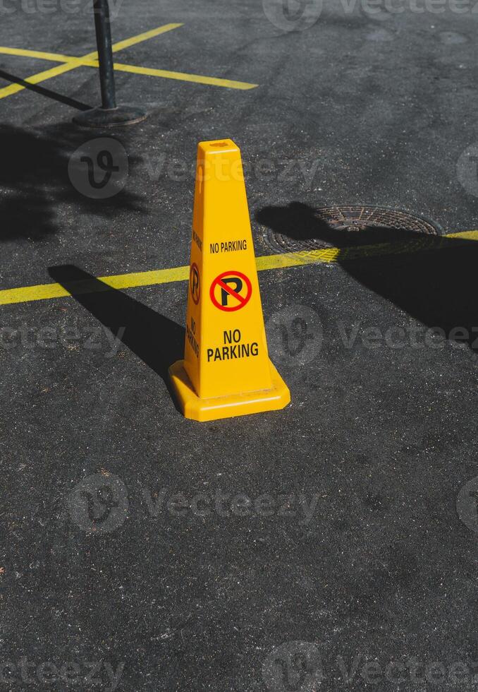 Yellow road cone with a warning not to park on a back of gray asphalt road. photo