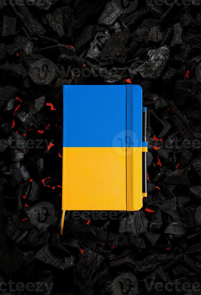 A small closed notebook with a yellow-blue cover in the colors of the Ukrainian flag. Texture of charcoal. Dark back photo