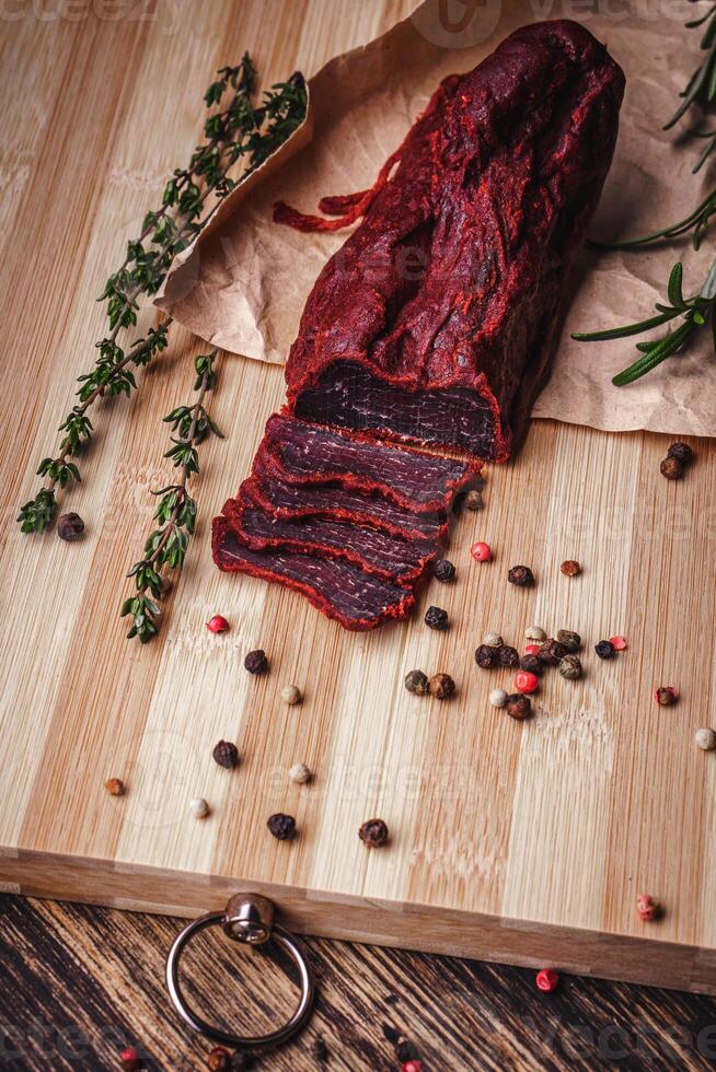 Close-up of basturma sliced into pieces. Dried meat with spices cut into slices. Dried horse meat on a wooden board with rosemary and caraway herbs photo
