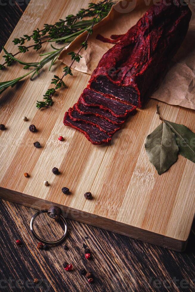 Close-up of basturma sliced into pieces. Dried meat with spices cut into slices. Dried horse meat on a wooden board with rosemary and caraway herbs photo