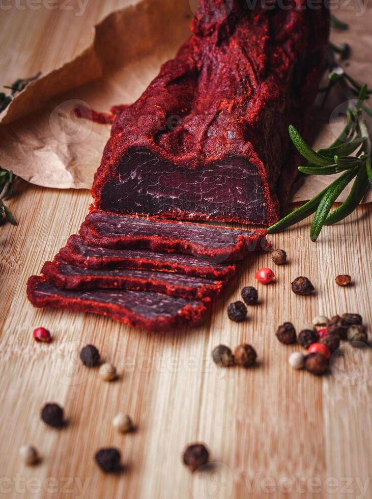 Close-up of basturma sliced into pieces. Dried meat with spices cut into slices. Dried horse meat on a wooden board with rosemary and caraway herbs photo