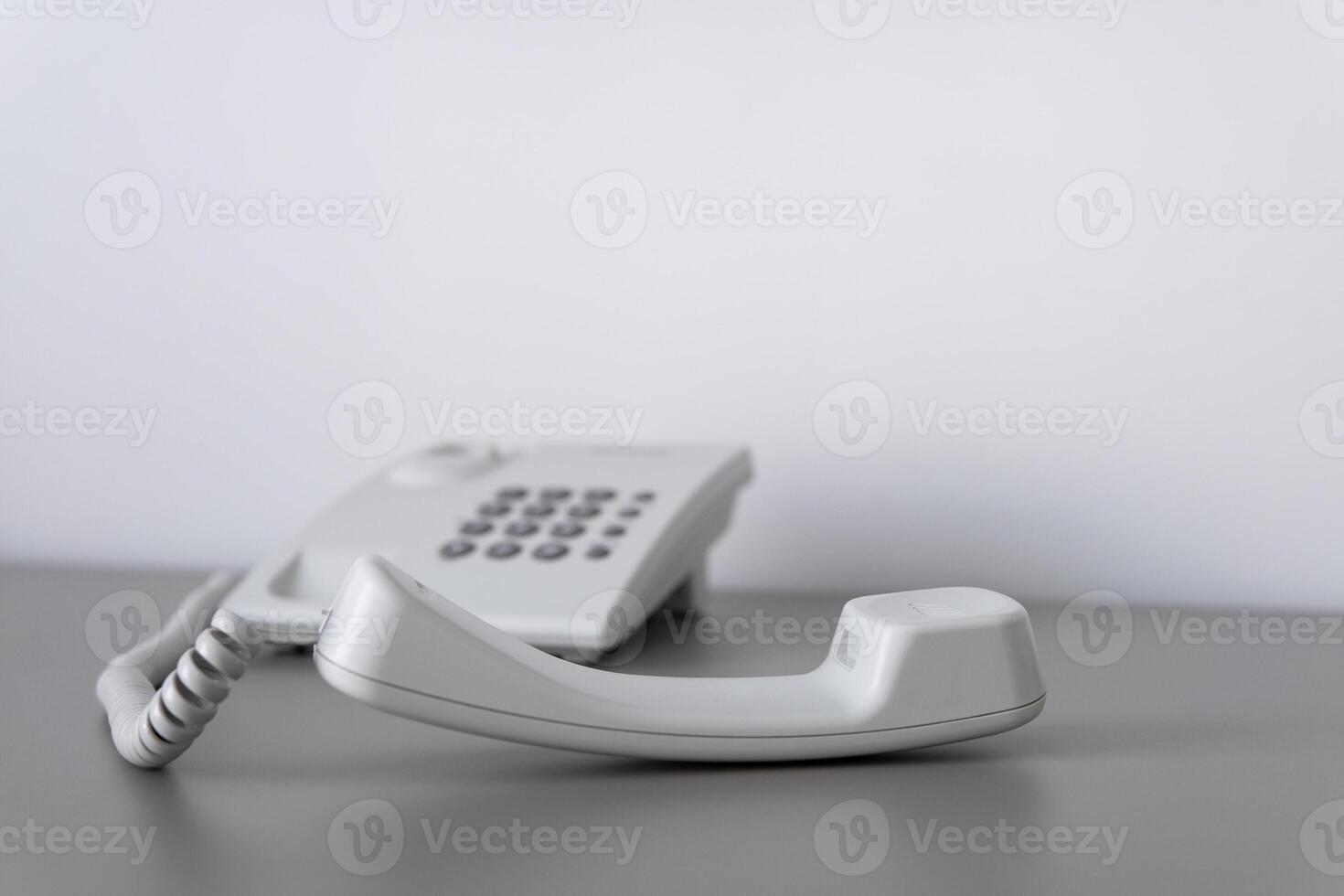 Modern white landline office phone with a hook. Technical support concept. No answer. Closeup white phone , office phone on the desk. Closeup white phone , office phone on the desk. photo