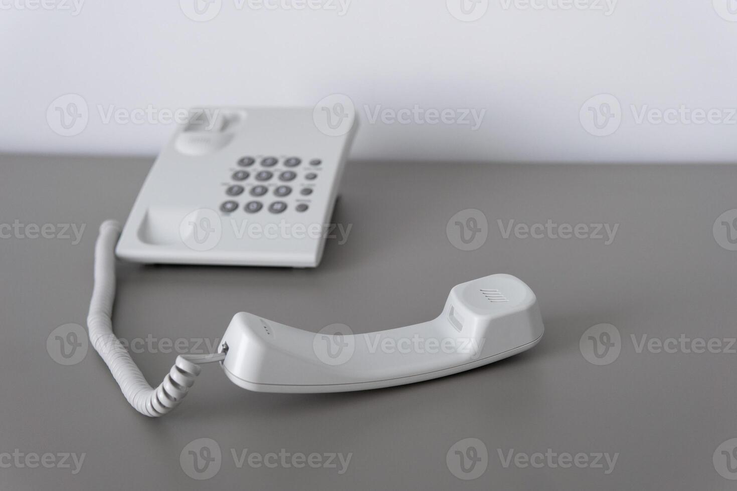 Modern white landline office phone with a hook. Technical support concept. No answer. Closeup white phone , office phone on the desk. Closeup white phone , office phone on the desk. photo