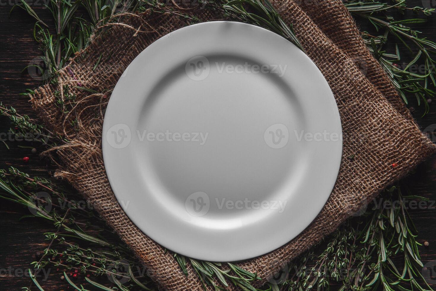 An empty plate in the middle of fragrant herbs on the table. Serving with thyme and rosemary burlap. Breakfast lunch or dinner in a rustic style photo