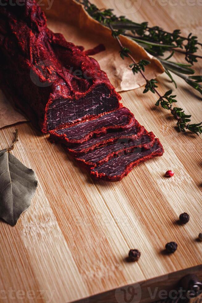 Close-up of basturma sliced into pieces. Dried meat with spices cut into slices. Dried horse meat on a wooden board with rosemary and caraway herbs photo