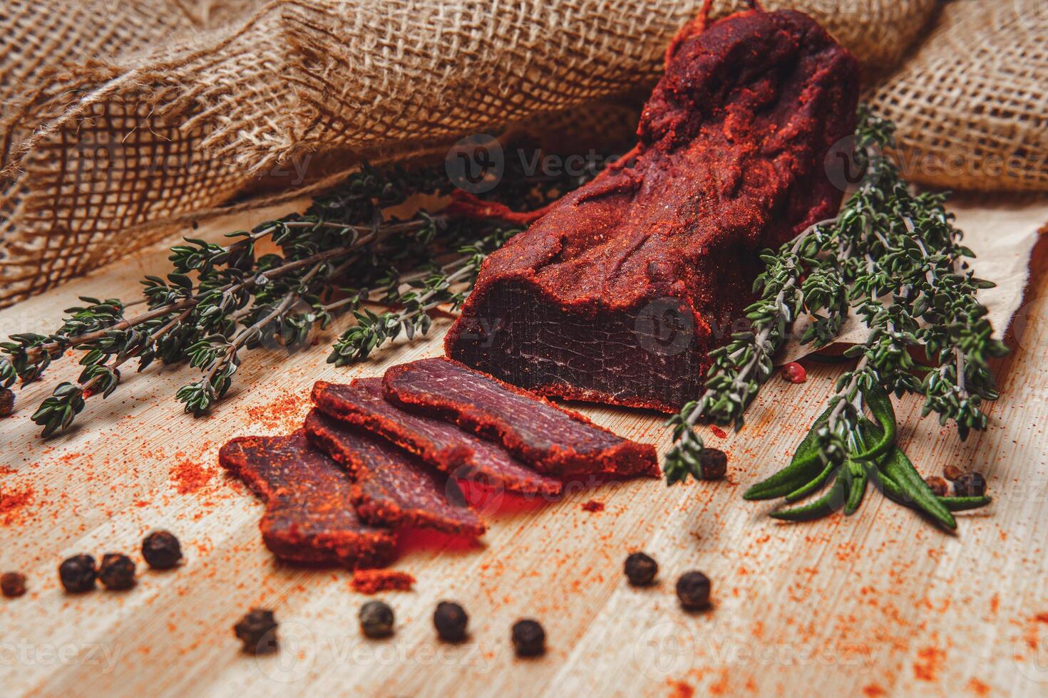 Close-up of basturma sliced into pieces. Dried meat with spices cut into slices. Dried horse meat on a wooden board with rosemary and caraway herbs photo