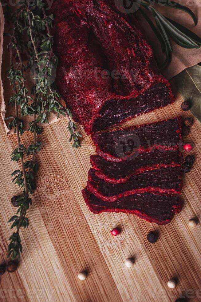 Close-up of basturma sliced into pieces. Dried meat with spices cut into slices. Dried horse meat on a wooden board with rosemary and caraway herbs photo