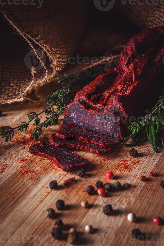 Close-up of basturma sliced into pieces. Dried meat with spices cut into slices. Dried horse meat on a wooden board with rosemary and caraway herbs photo