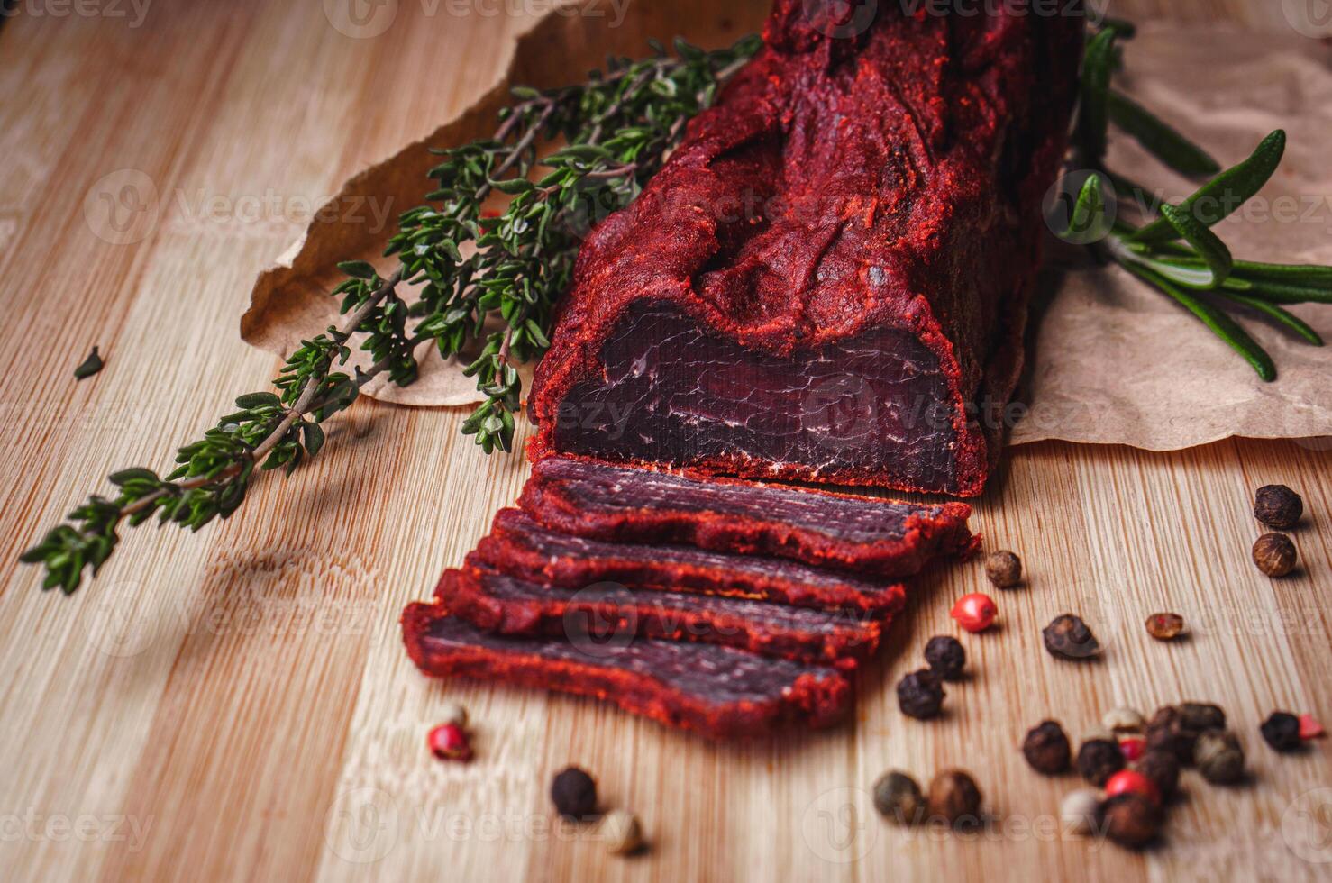 Close-up of basturma sliced into pieces. Dried meat with spices cut into slices. Dried horse meat on a wooden board with rosemary and caraway herbs photo