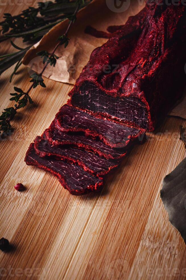 Close-up of basturma sliced into pieces. Dried meat with spices cut into slices. Dried horse meat on a wooden board with rosemary and caraway herbs photo