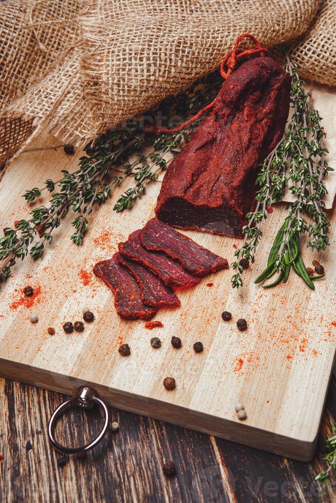 Close-up of basturma sliced into pieces. Dried meat with spices cut into slices. Dried horse meat on a wooden board with rosemary and caraway herbs photo